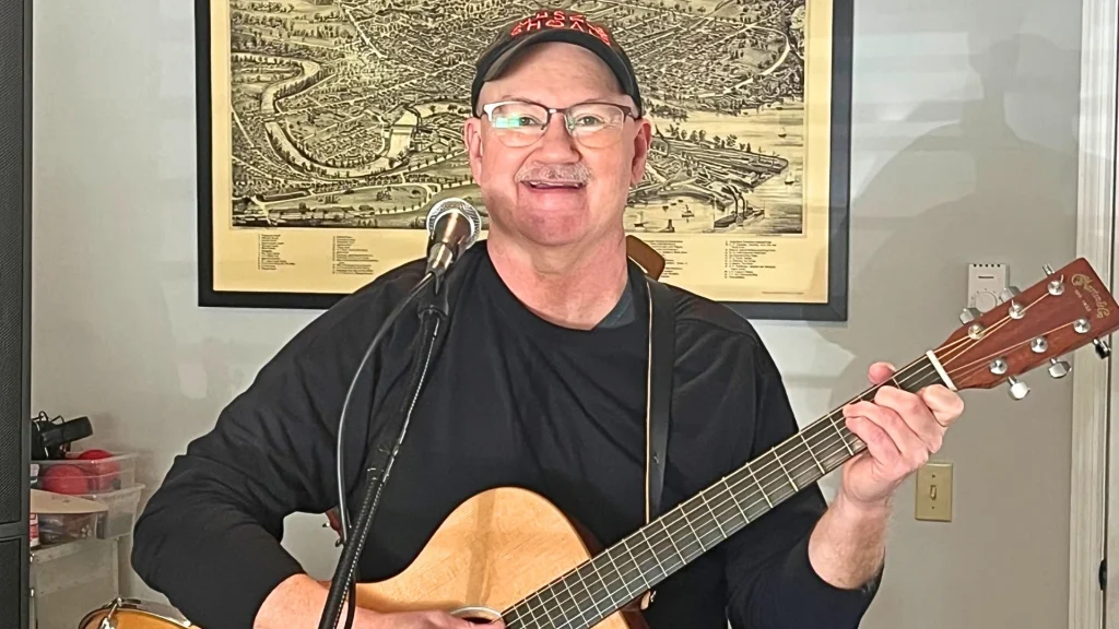 JB Guay playing acoustic guitar and singing into a microphone during a live music performance.