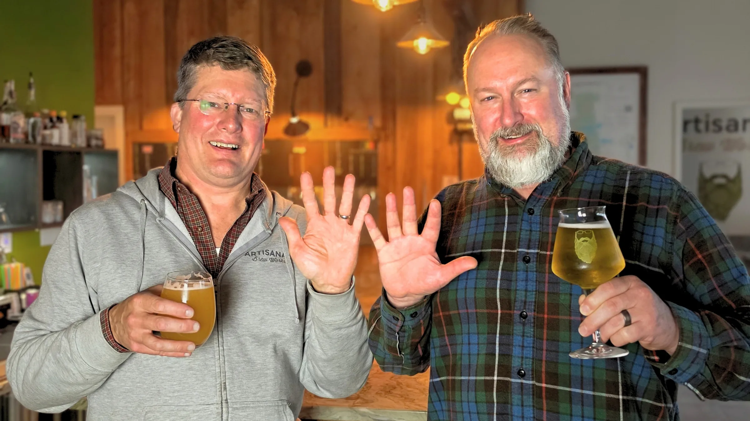 Artisanal Brew Works owners holding beers and raising ten fingers for the 10-year anniversary celebration in Saratoga Springs, NY.